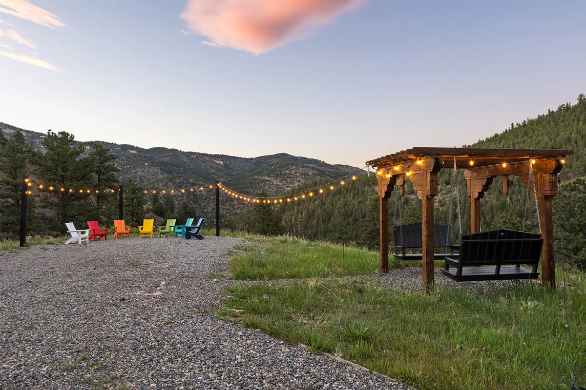 A single string of lights are strung around a set of brightly colored Adirondack chairs with an unimpeded view of the mountains at at Hummingbird Hill in Colorado.