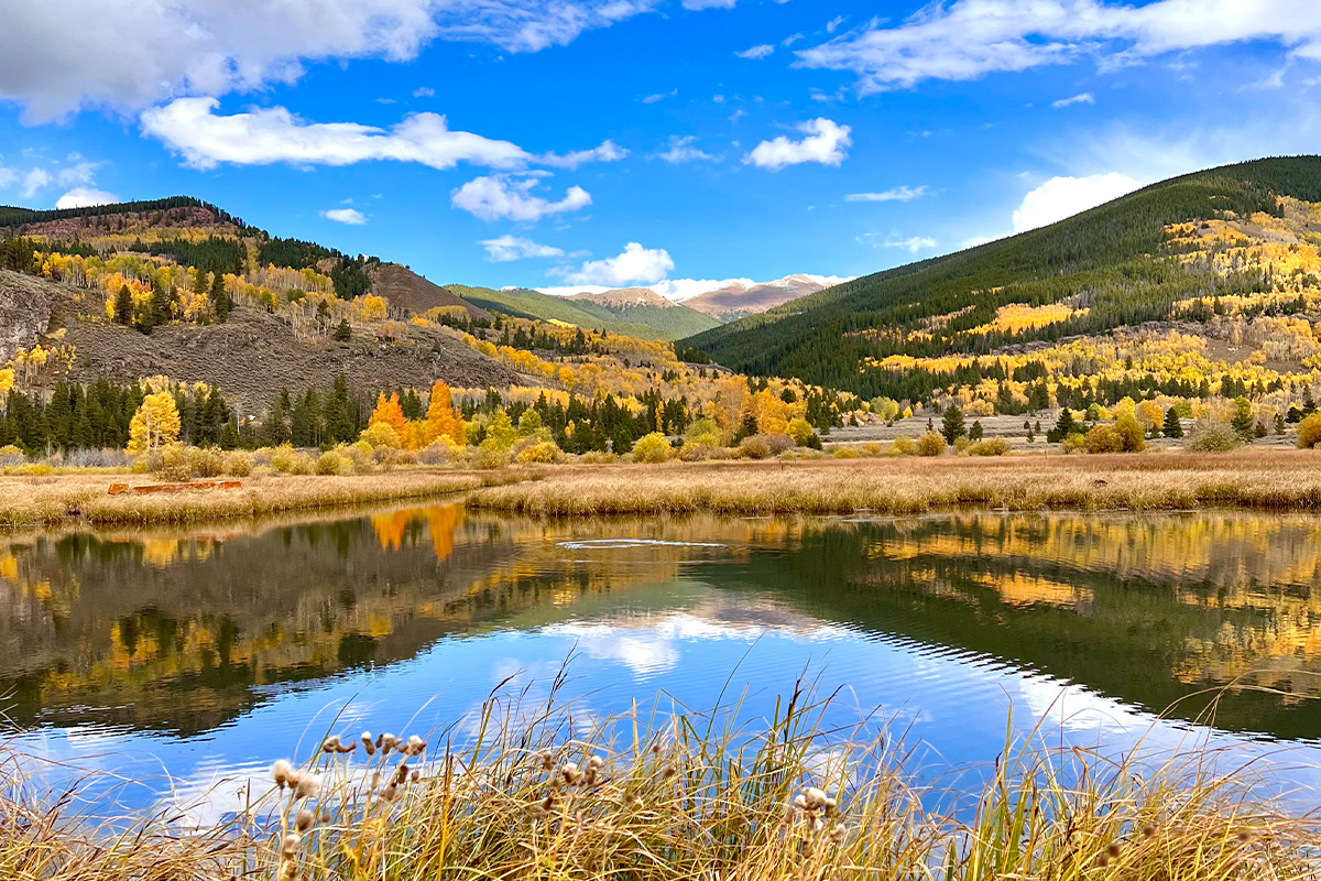 The vibrant colors of the Rocky Mountains in autumn are reflected in the mirror-like surface of the lake near Camp Hale in Colorado.