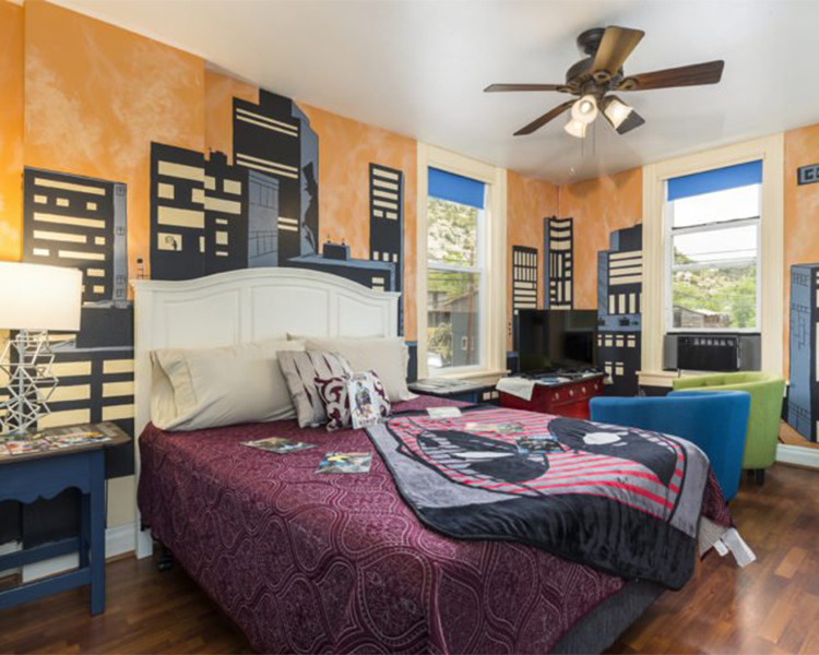 A guest room at Ore House Inn in New Castle is painted sunset orange with the silhouette of a cityscape. The bed has red sheets and comic books on it.