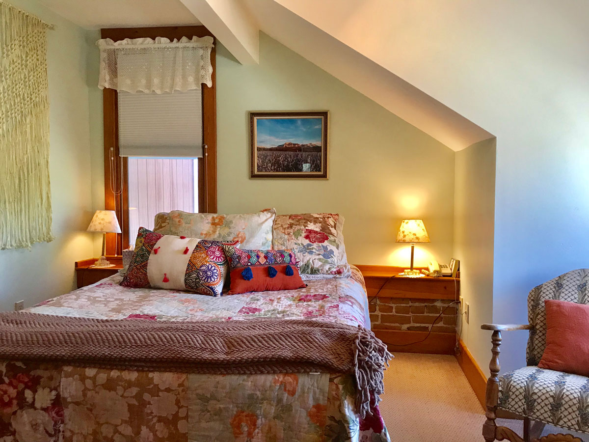 The Bross's Apricot Bliss Room is your home away from home with subtle, warm lighting and a cozy bed covered in throw pillows.