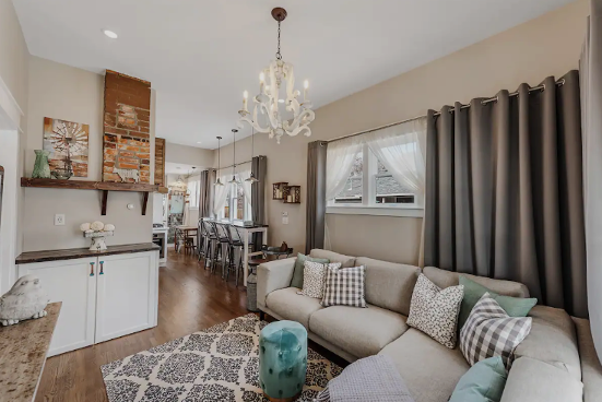 The Aggie House in Lousiville features an expansive couch in its living room along with a stylish chandelier