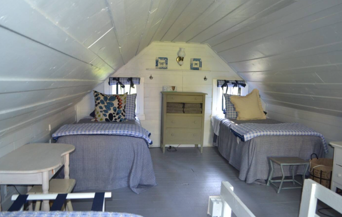 Two twin beds are placed under an arched ceiling on the upper floor of The Butterfly, a simple cabin in the woods.
