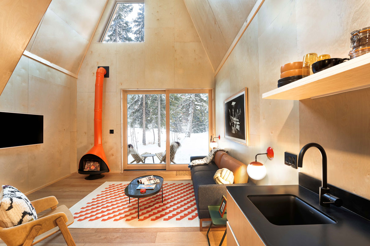 The interior of an A-Frame Club cabin is bright and cheery, with an orange wood-burning stove and a equipped kitchen.