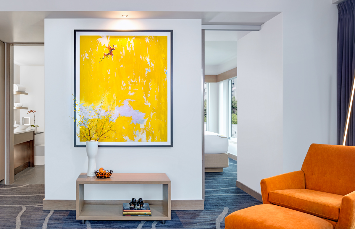The Art's Museum Suite living room features a bright yellow framed painting and a plush orange chair.