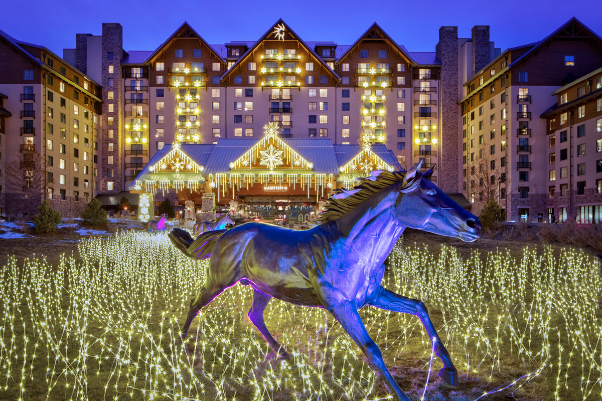 Gaylord Rockies Resort & Convention Center seen from the exterior with holiday lighting. A galloping horse statue is in the foreground.