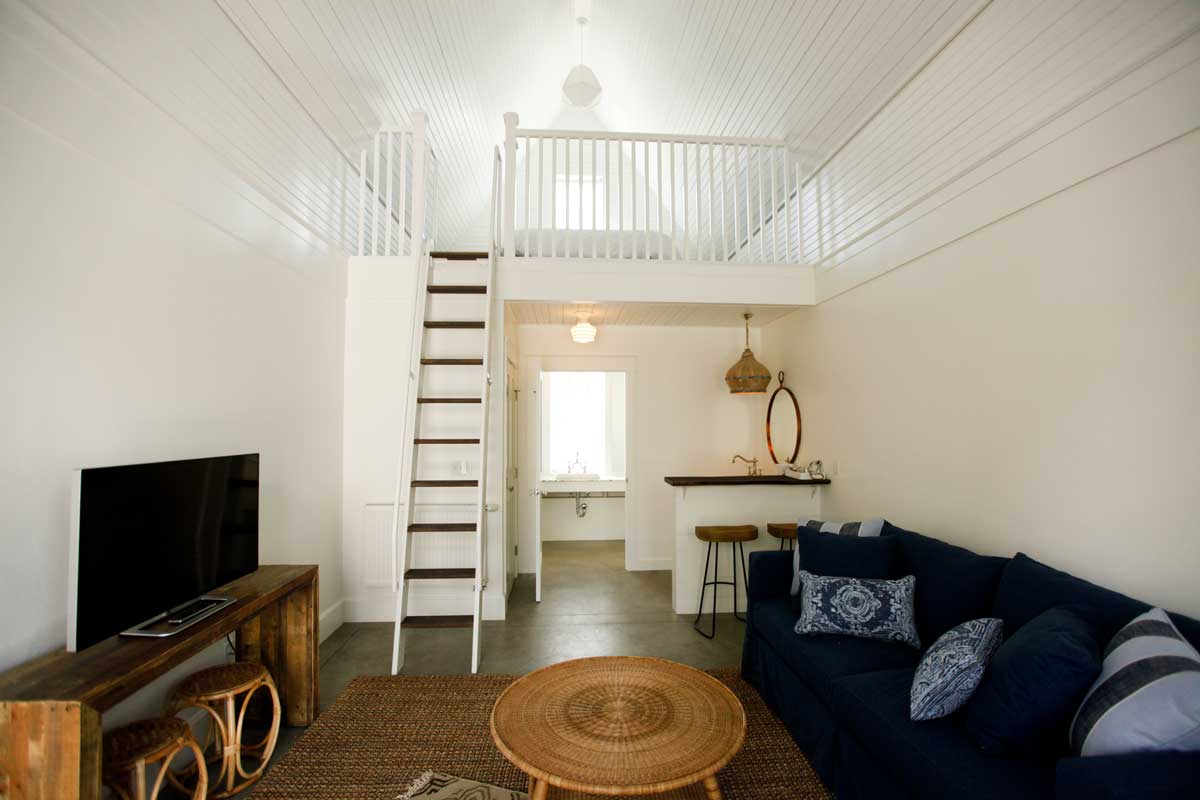 This room at the Surf Hotel features a loft bed and kitchenette space. The room is white and filled with bright natural light.