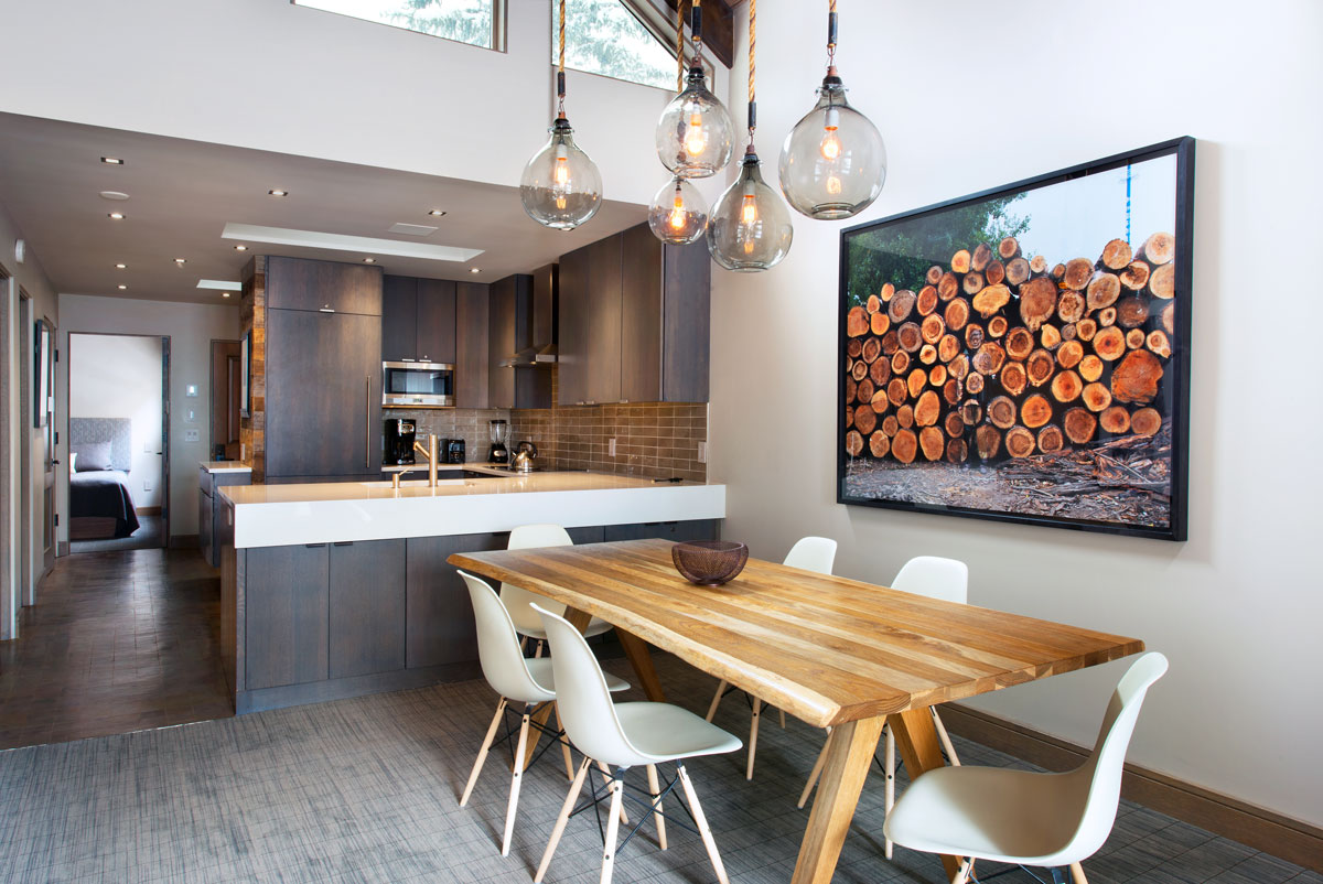 A condo-style kitchen and dining room at The Gant, featuring stylish pendant lighting and a long burnished-wood dining table