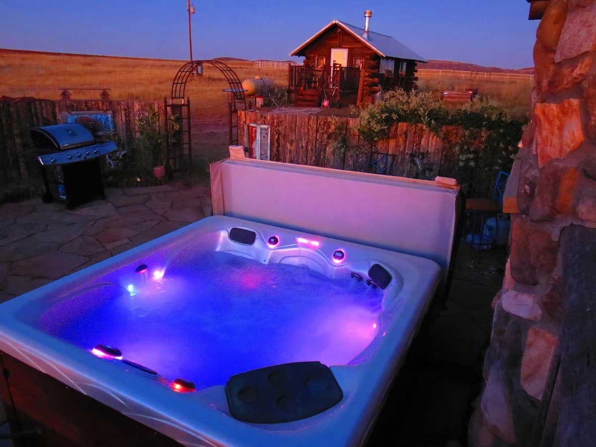 The hot tub is just thirty steps away from the Colorado Cabin Escape. Lights in the hot tub glow purple.