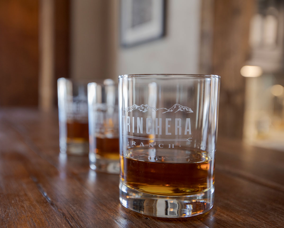 Whiskey in fancy Trinchera Blanca Ranch glasses sitting on a wooden bar