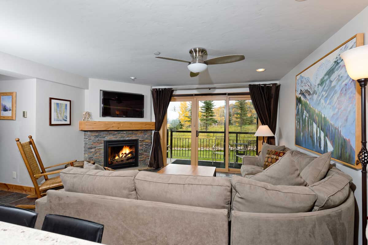 A cozy stone fireplace and gray sectional couch add a cozy touch to a living room at The Crestwood Condominiums in Snowmass.