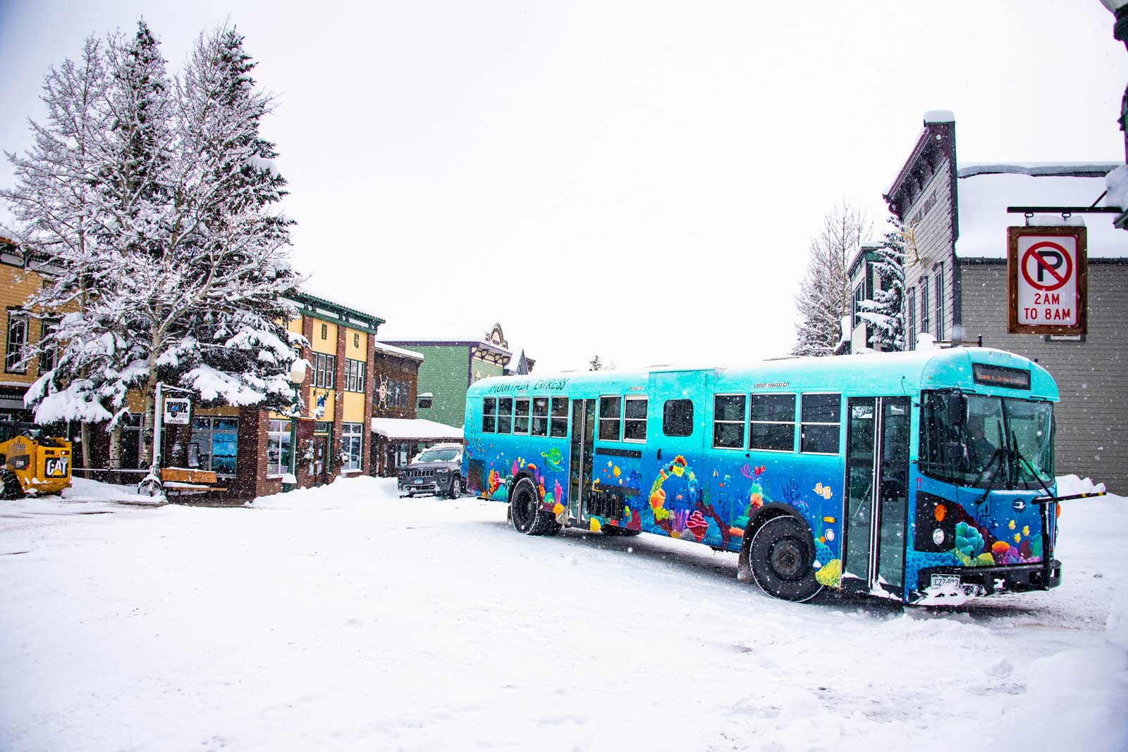 A bright blue Mountain Express town shuttle drives down Elk Avenue in the snow