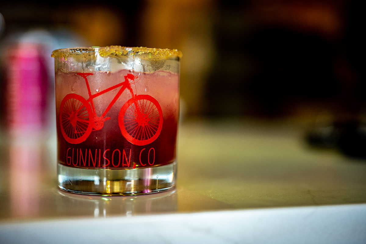 Red cocktail in a short glass that has a bicycle design and wording that reads "Gunnison, CO" on it
