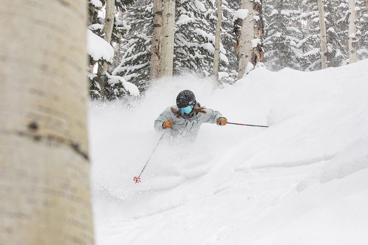 Skier with deep snow spraying around her amid trees