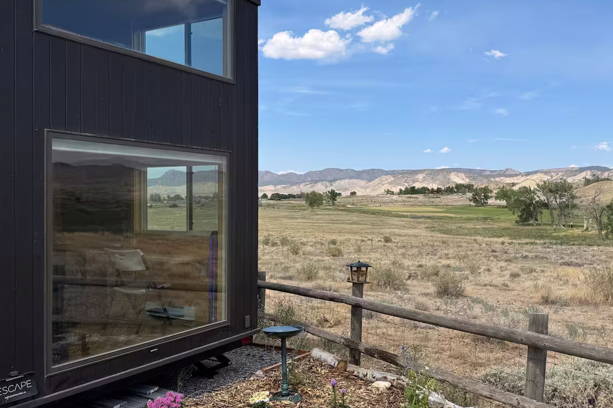 The side of a tiny house in Montrose, Colorado, shows massive windows for an office space that looks out onto an expansive landscape.