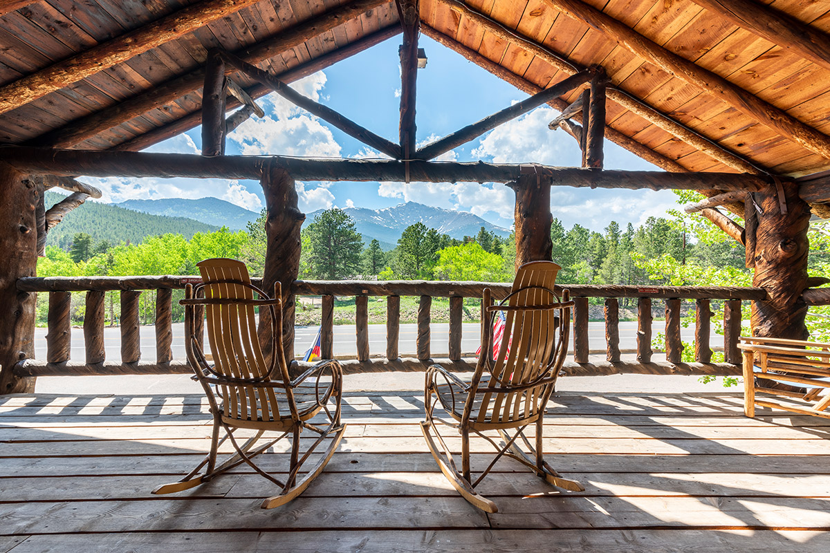 Two rocking chairs sit on a roofed balcony at Meeker Park Lodge with a unobstructed view of towering Rocky Mountain peaks.
