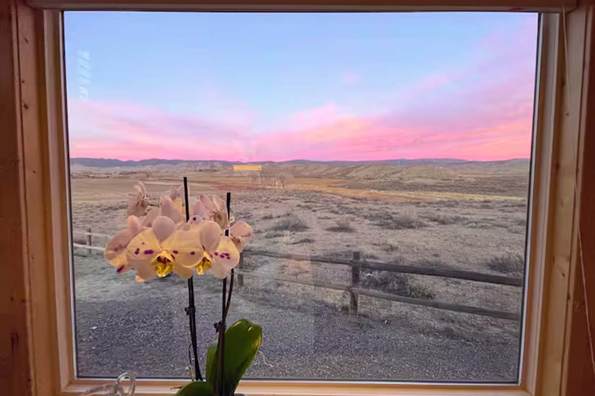 A tie-dye sunset of pink, purple and blue paints the sky outside a window of a tiny home in Montrose, Colorado.
