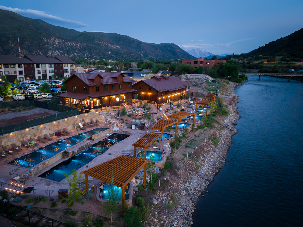 An aerial view of Iron Mountain Hot Springs with warm lights glowing and stunning teal-blue hot springs. 