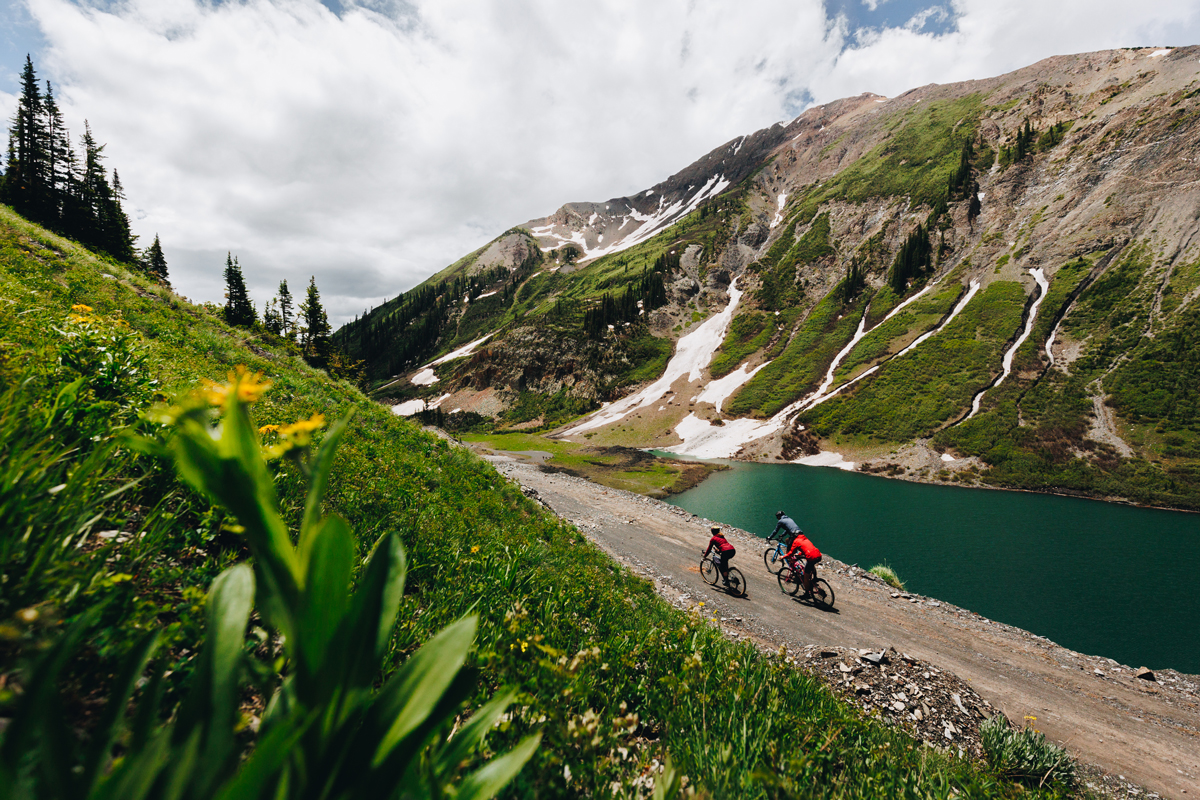 Gravel bikers ride a trail alongside the green waters of Emerald Lake in Crested Butte, Colorado