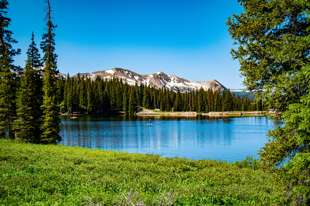 A person paddleboards on the shining blue waters of Lake Irwin with mountains rising in the background in Crested Butte, Colorado.