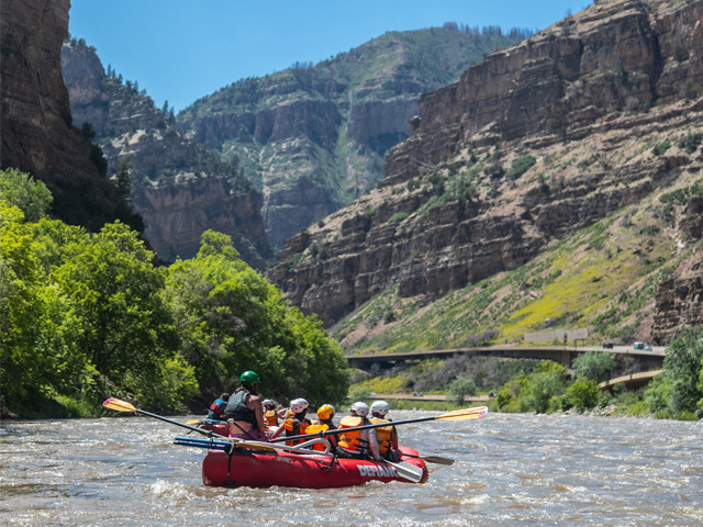 A group of people on a red raft riding through a calm section of Glenwood Canyon in Glenwood Springs, Colorado