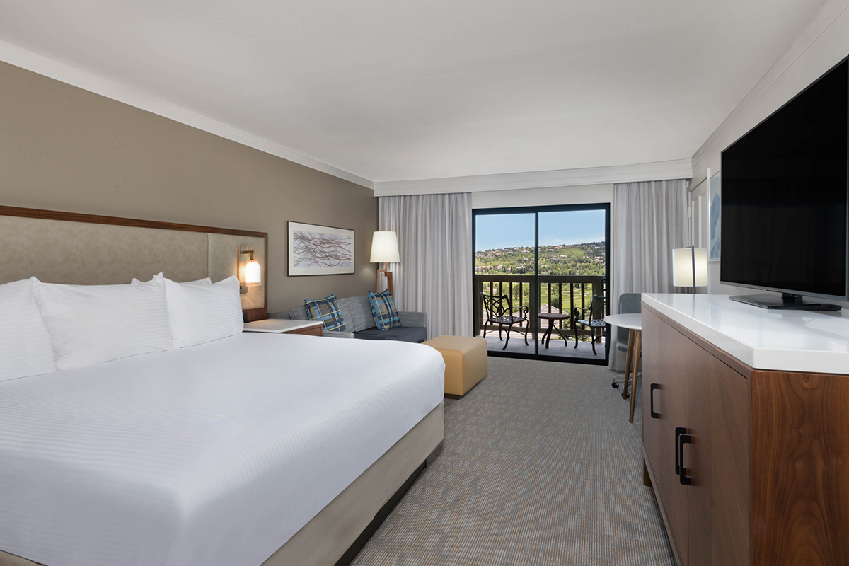 A guest room at Cheyenne Mountain Resort has chic and cozy furnishings along with a verdant view outside the balcony door.