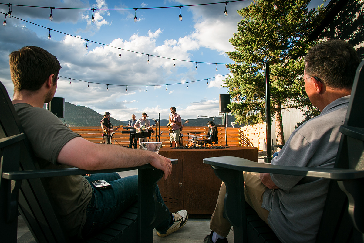 Two people lounge in Adirondack chairs as they listen to a band play on a small nearby stage at LOGE Wolf Creek.