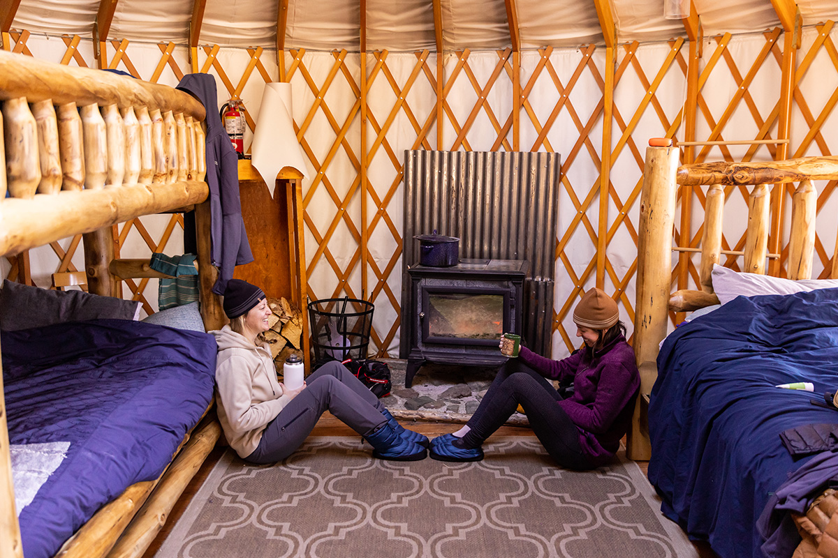 Two adults sit on the floor inside a yurt with wooden lattices along the walls near Leadville, Colorado.