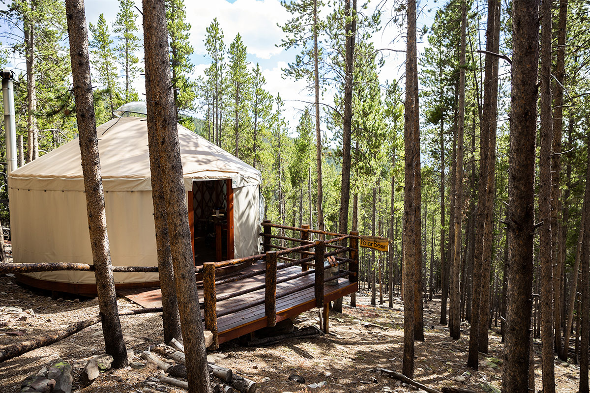 A canvas-covered yurt near Leadville, Colorado, sits on a wooden deck surrounded by tall pine trees.