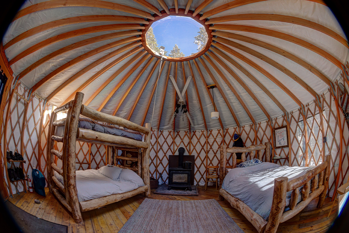 The inside of a yurt at Tennessee Pass Sleep Yurts features two bed sets made of logs, a stove and ski-themed decor.