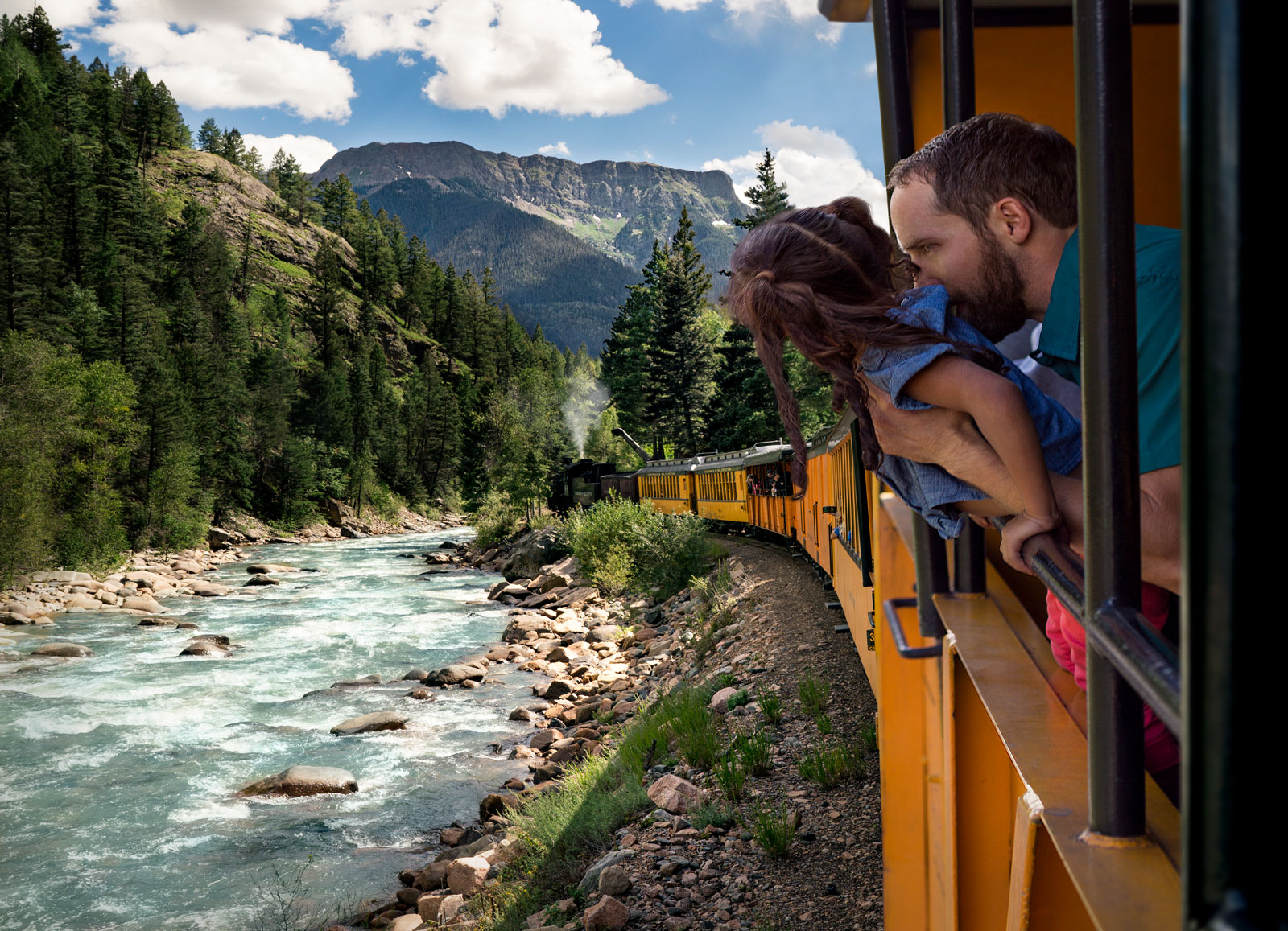 A man and his daughter look out from the Durango train onto the river