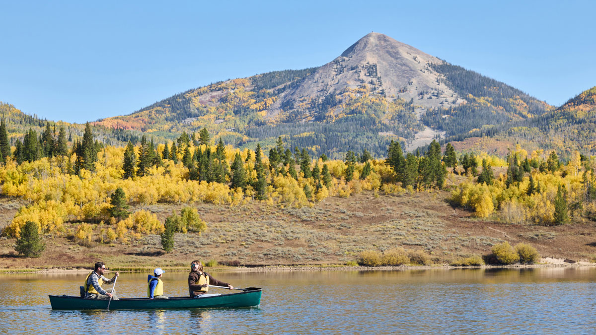 Family canoeing on Pearl Lake near Steamboat Springs, surrounded by fall-colored trees and mountains in the background.