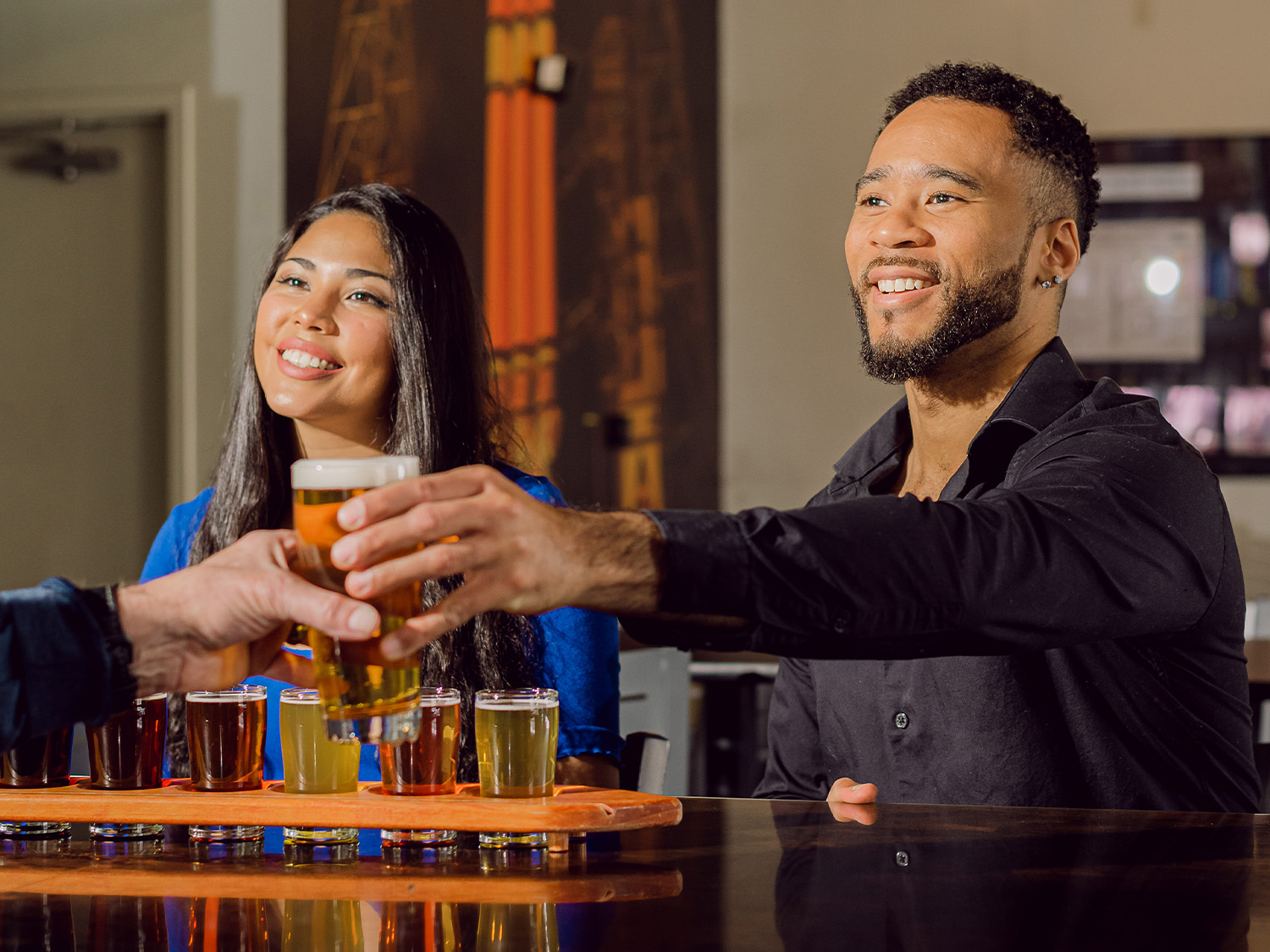 One person smiles over a flight of beers of varying hues while another takes a full pint from a bartender at Launch Pad Brewery in Aurora, Colorado.