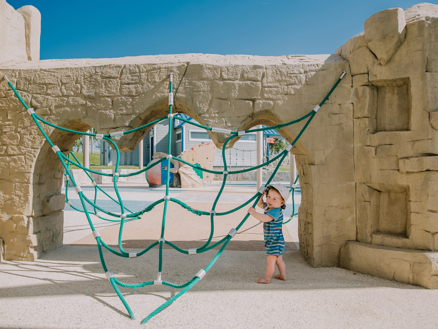A blond toddler grabs on to a turquoise net a playground in Aurora, Colorado. 