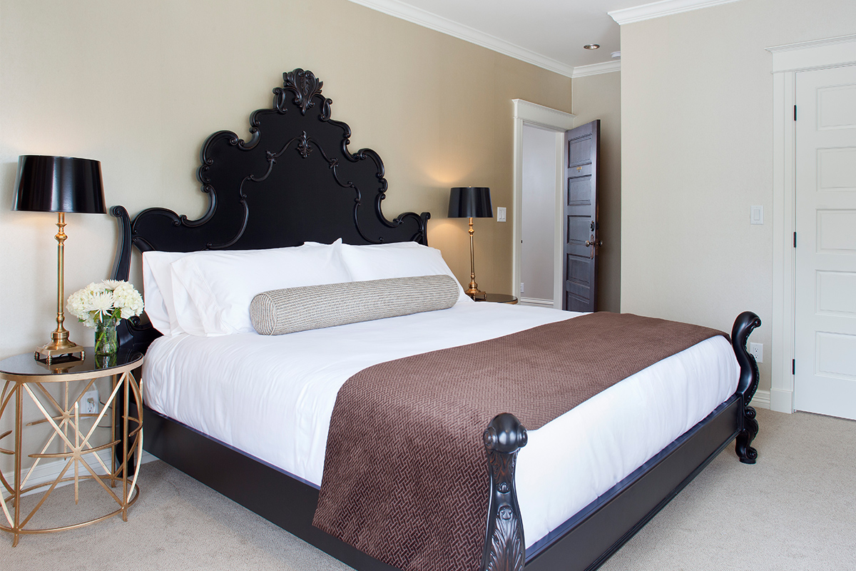 A large, dark wooden bed with an intricately carved headboard awaits guests in the Avery Room at Edwards House in Fort Collins.