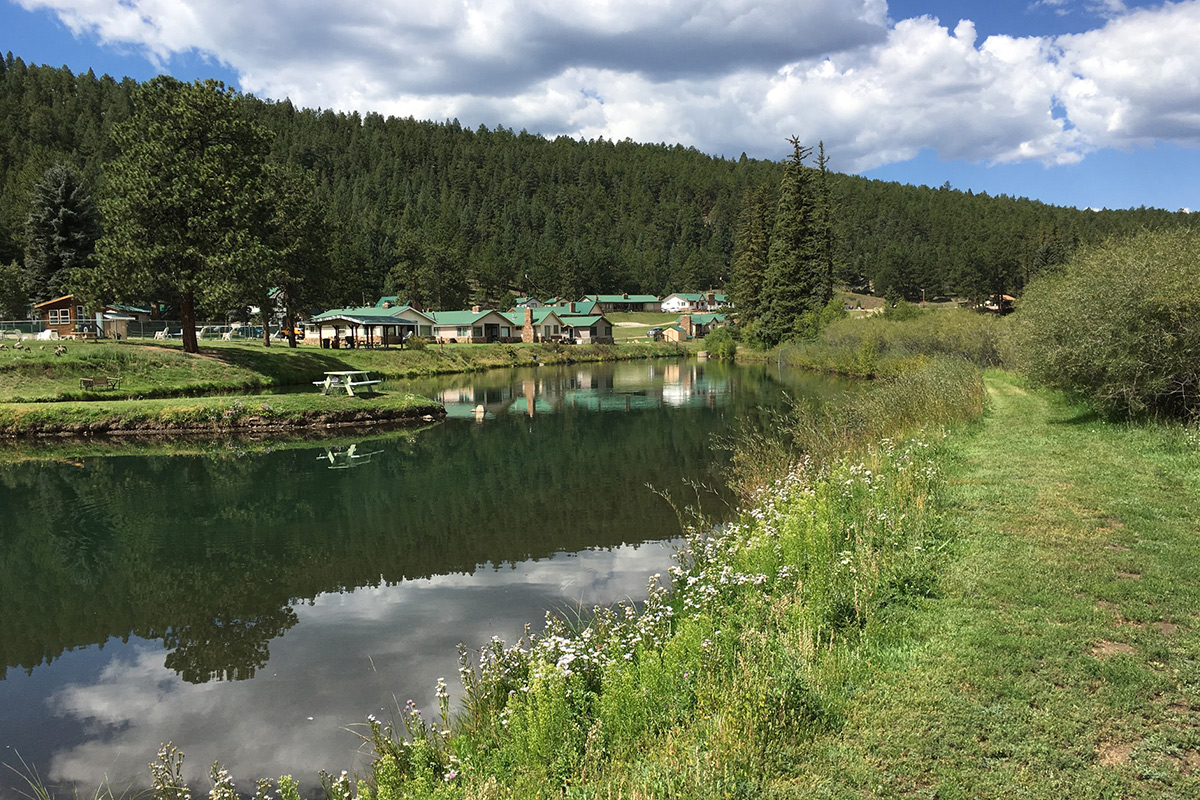 A large, reflective pond lays out alongside the units of the Bailey Lodge in Bailey, Colorado.