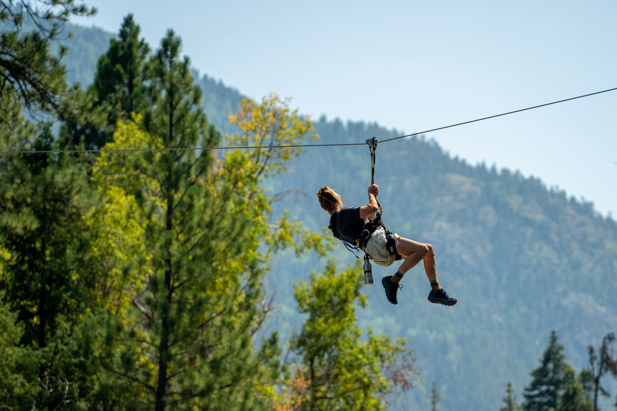 A woman ziplining through the treetops, staring out at the forest views in Colorado.