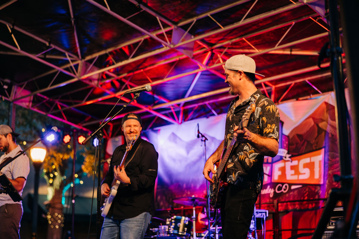Smiling band members performing under stage lights at Greeley Friday Fest in Colorado.