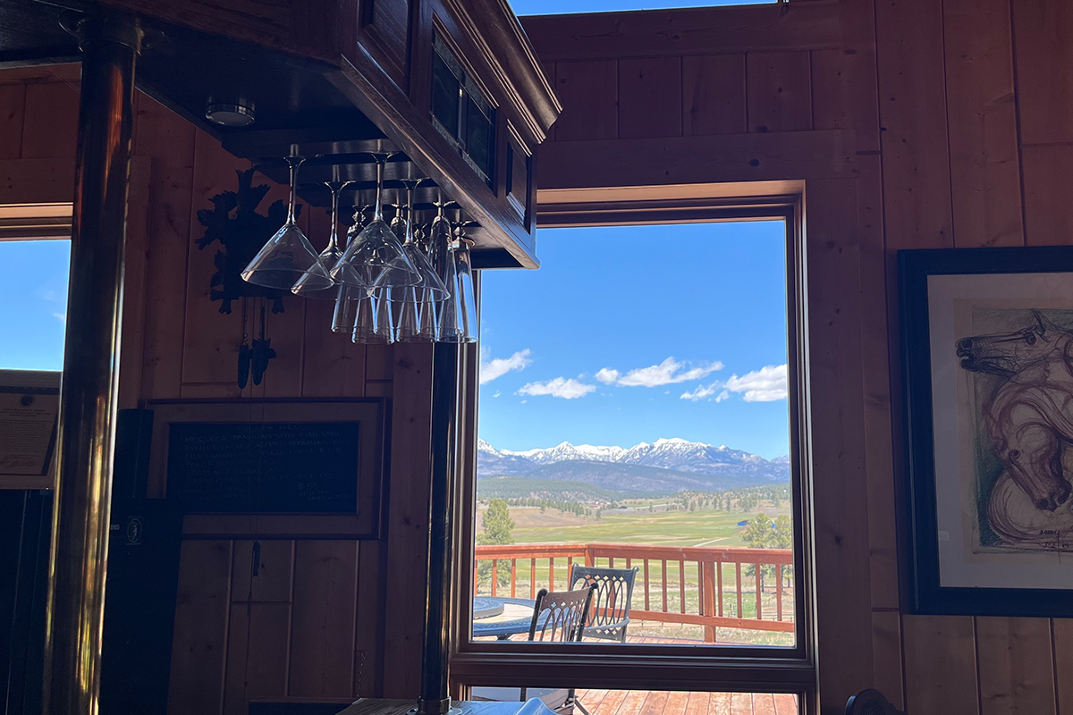 Through the window in a common area space at Elkwood Manor Bed & Breakfast, you can see green open pastures and towering, snowy mountain peaks.