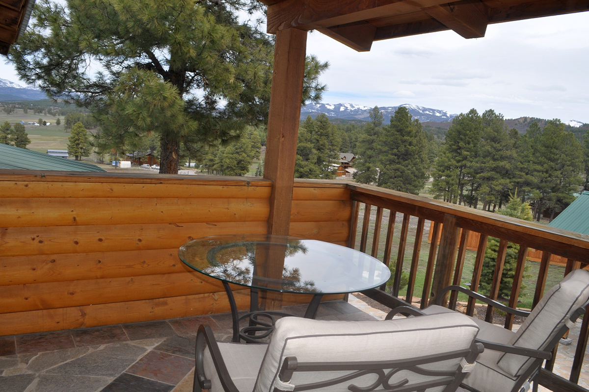 A pine forest offers a beautiful landscape to look out on from a private balcony space complete with chairs and a table at the Elkwood Manor Bed & Breakfast in Colorado.