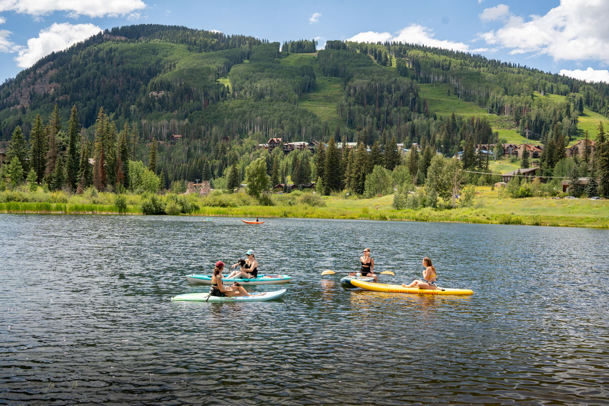 Friends paddling across a still lake with greenery and rolling slopes in the background.