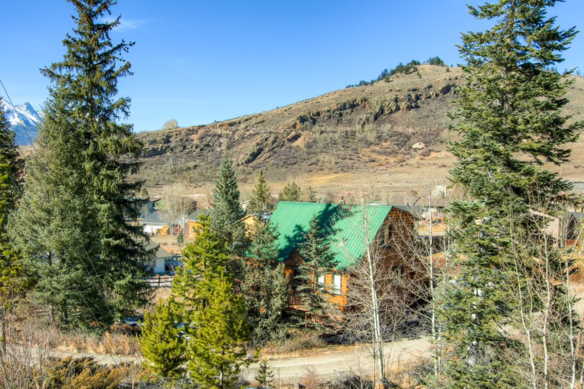 Tall pines, rolling foothills and towering mountains streaked with white surround a cabin with a bright green roof in Dillon, Colorado.