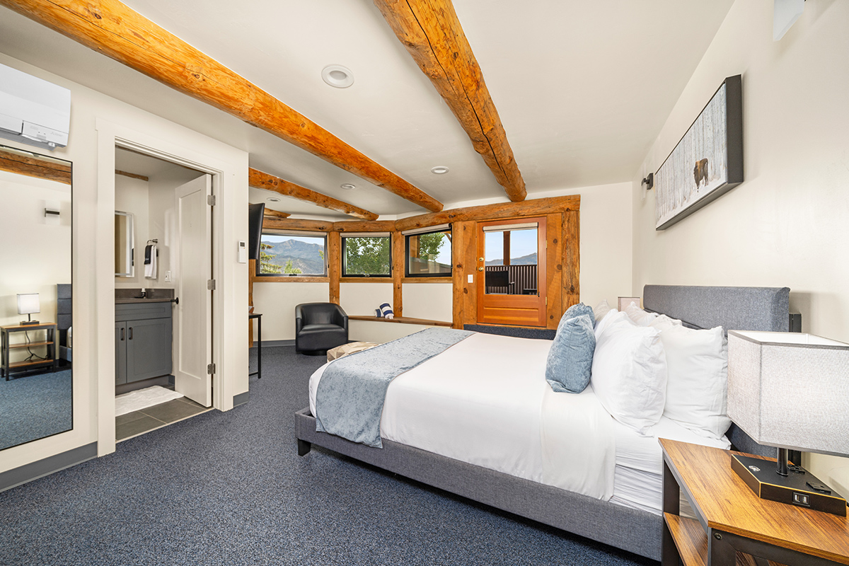 An updated guest room at the Chipeta Lodge Resort +Spa in Ridgway, Colorado, features stunning views, a balcony and exposed wooden beams.