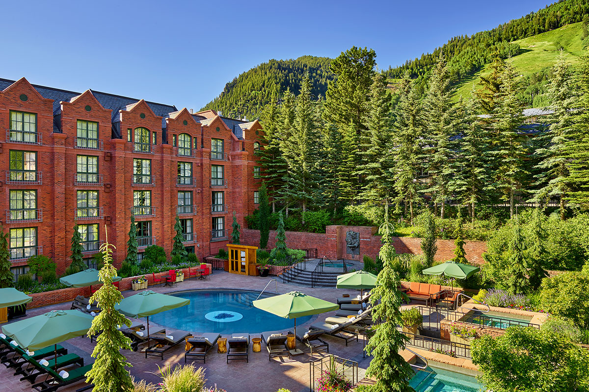 An aerial view of the St. Regis Aspen Resort shows a stone courtyard with multiple pools surrounded by towering pines.