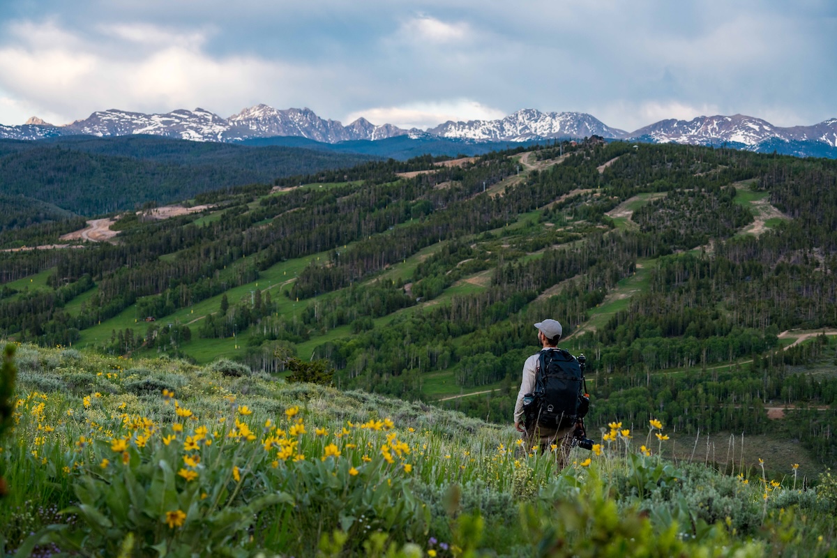 A hiker with a backpack looks out over green hills and snow-capped mountains near Granby, Colorado.