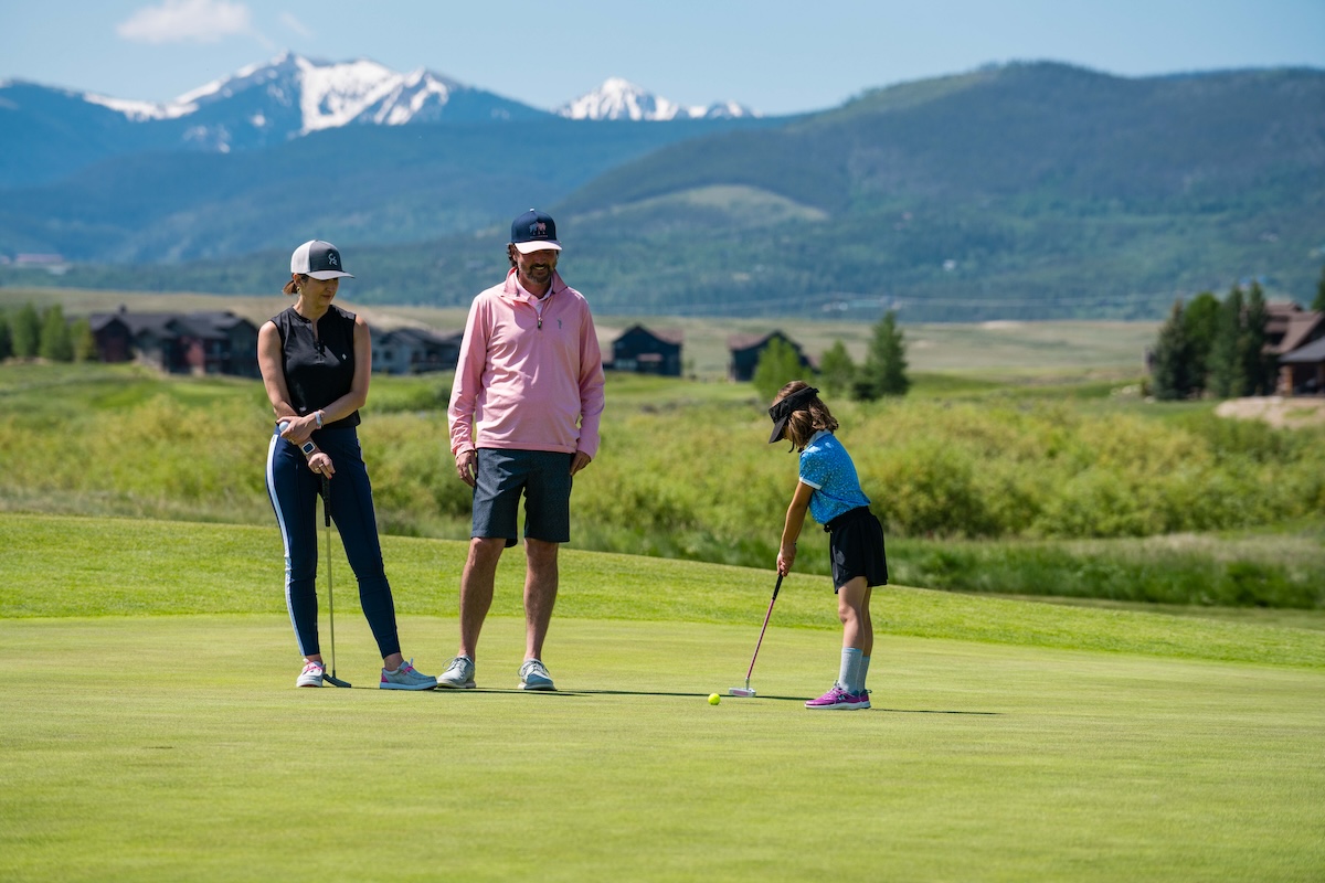 Family golfing on a green course with mountains in the background near Granby, Colorado.