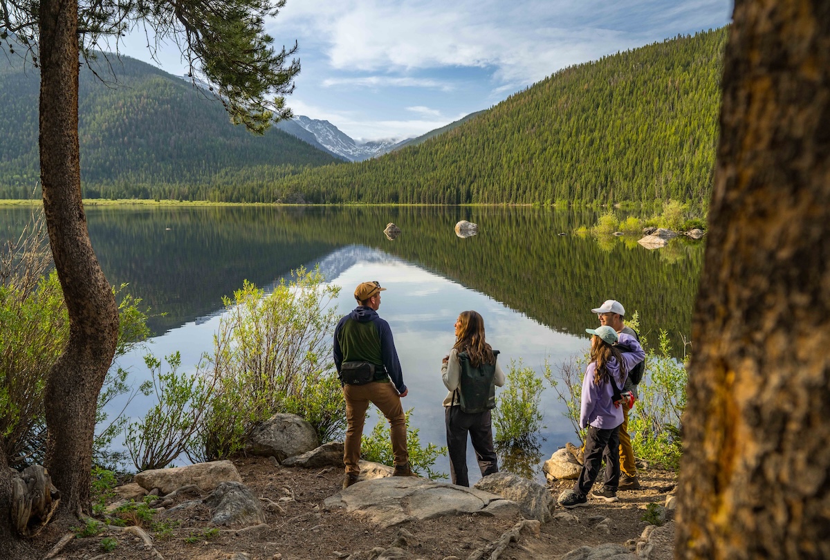 Adults standing beside a large lake reflecting forested hills near Granby, Colorado.