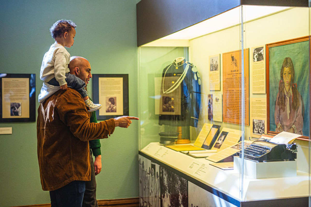 A father holding a child points to a history exhibit inside the Colorado Springs Pioneers Museum.