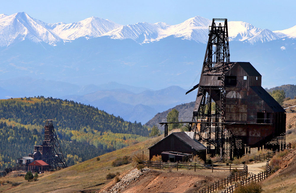 A historical wooden gold mine on Vindicator Valley Trail in Cripple Creek, Colorado with snow-capped mountains in the background. 