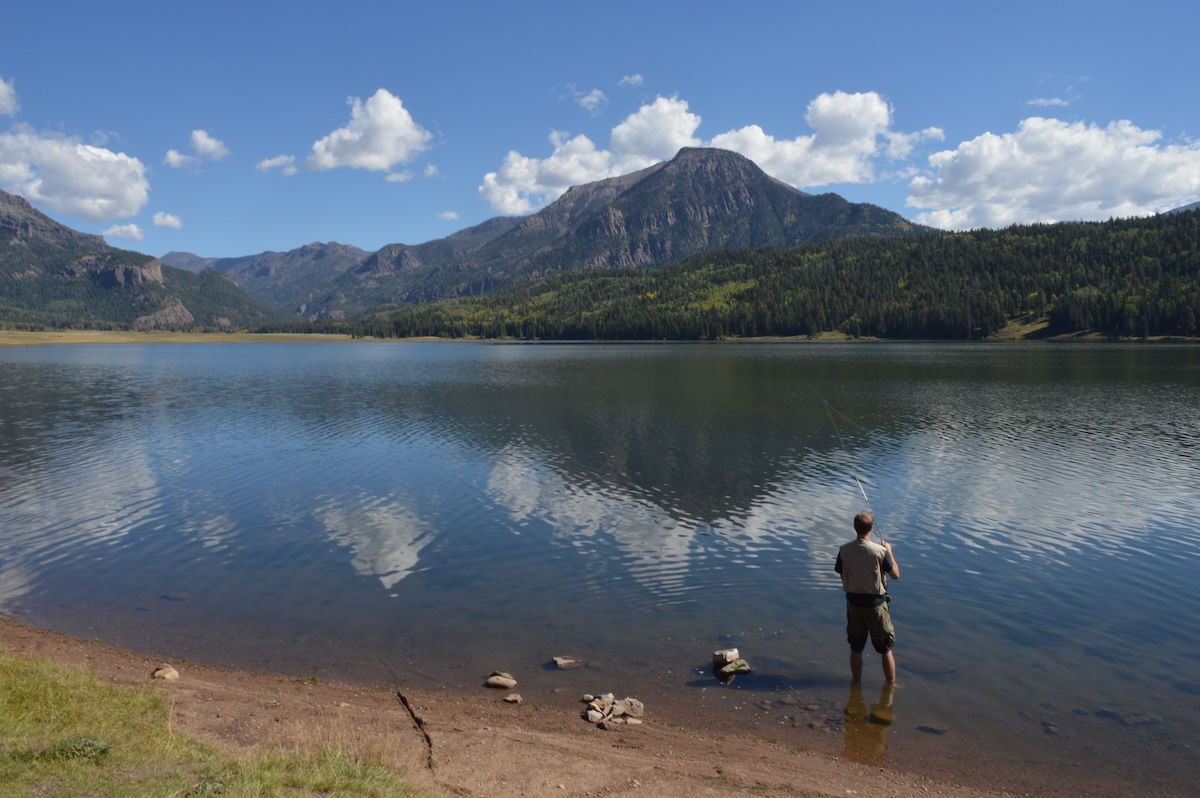 Man fishing from the shoreline with mountains in the background near Pagosa Springs, Colorado.