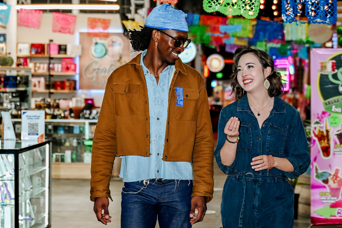 Two people walk through a colorful indoor market filled with shops and decorations in Aurora, Colorado.